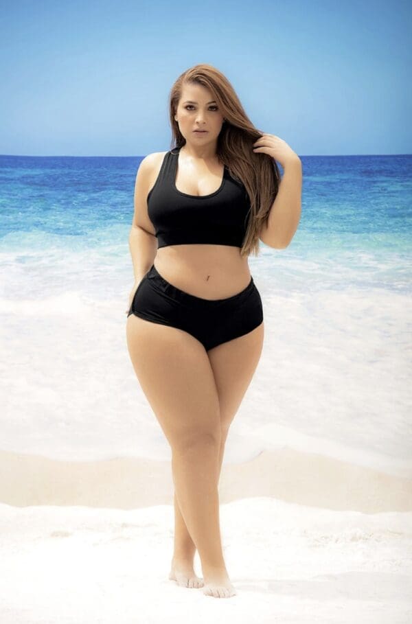 A woman in black bikini standing on the beach.