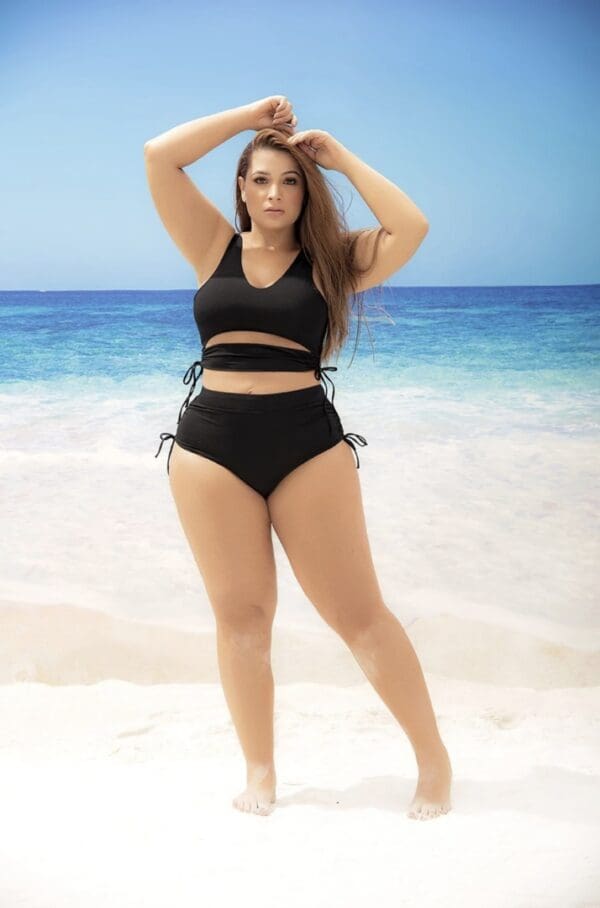 A woman in black swimsuit standing on the beach.