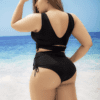 A woman in black swimsuit standing on the beach.