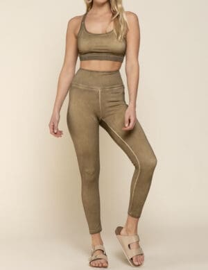 A woman standing in front of a wall wearing brown pants and a bra.