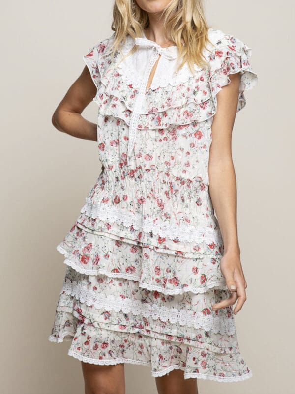 A woman in floral print dress standing next to wall.