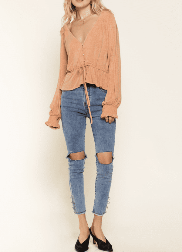 A woman wearing ripped jeans and an orange top.