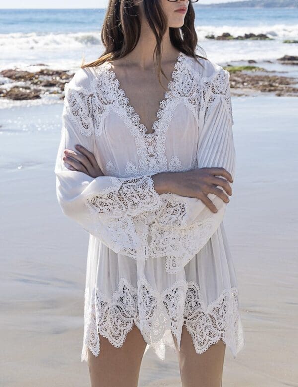 A woman standing on the beach wearing a white dress.