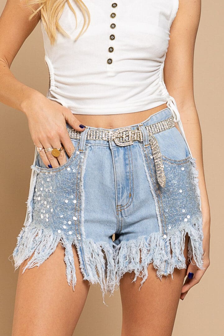 A woman wearing denim shorts with sequins and fringes.