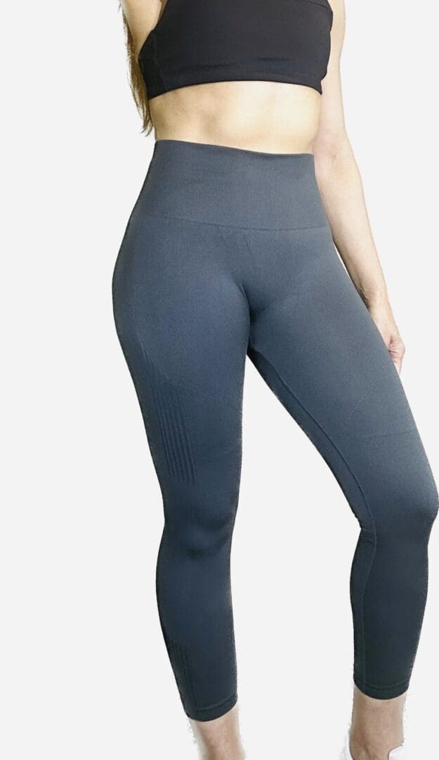 A woman is wearing grey leggings and has her hands on the back of her legs.