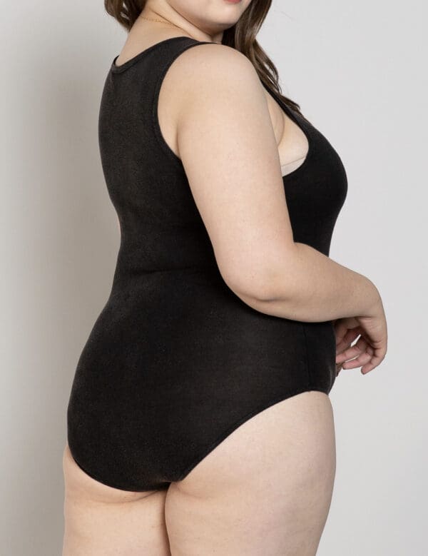 A woman in black bathing suit standing next to wall.