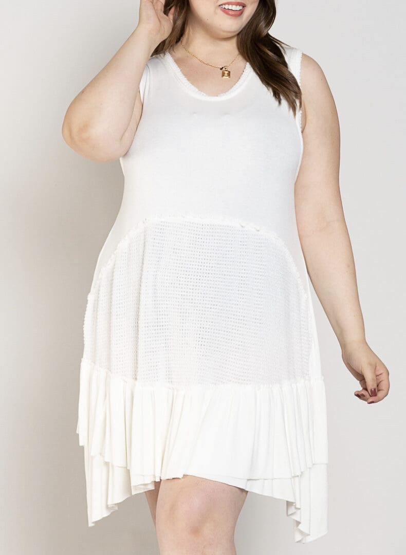 A woman wearing white dress standing next to wall.