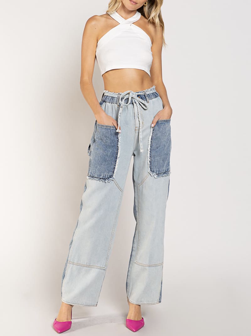 A woman wearing jeans and white top standing next to a wall.