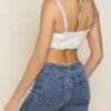 A woman wearing high waisted jeans and white bra top.