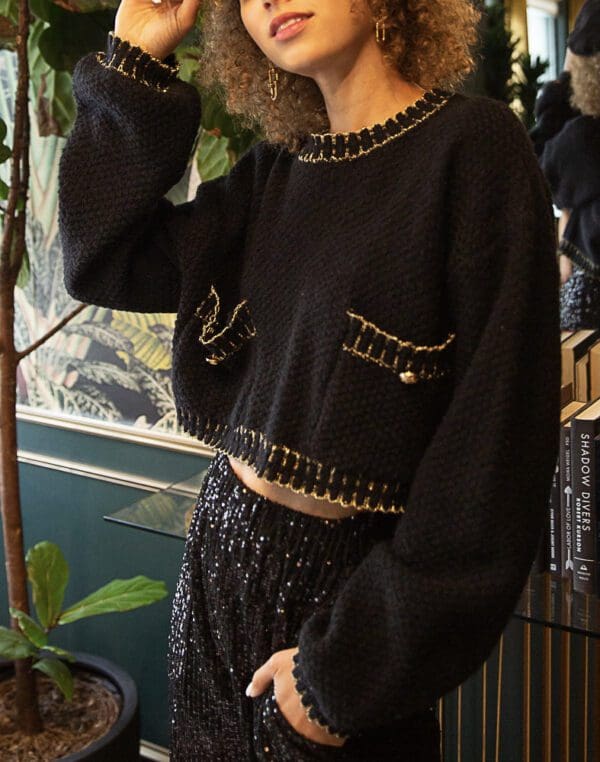 A woman in black sweater standing next to potted plant.