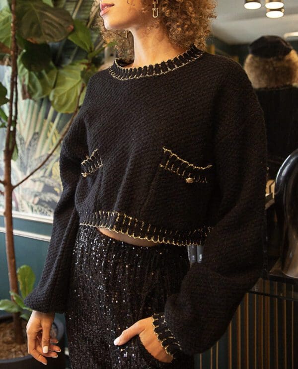 A woman in black sweater standing next to plant.