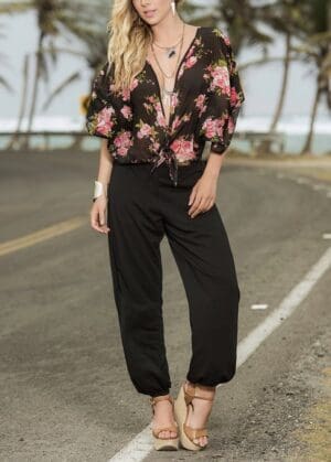 A woman in black pants and floral shirt standing on the side of road.