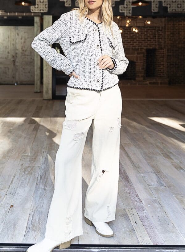 A woman in white pants and jacket standing on a wooden floor.