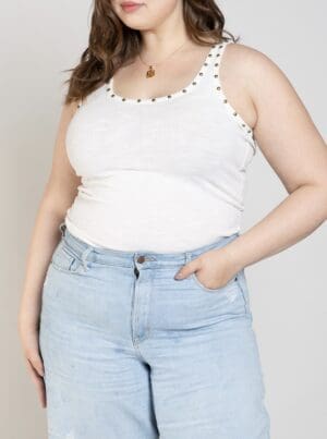 A woman wearing light blue jeans and white tank top.