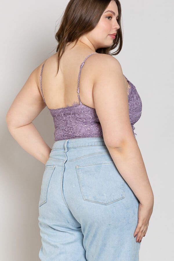 A woman wearing high waisted jeans and purple lace top.