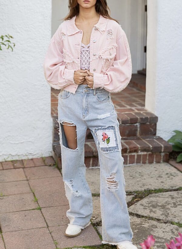 A person standing on the sidewalk wearing jeans and a jacket.