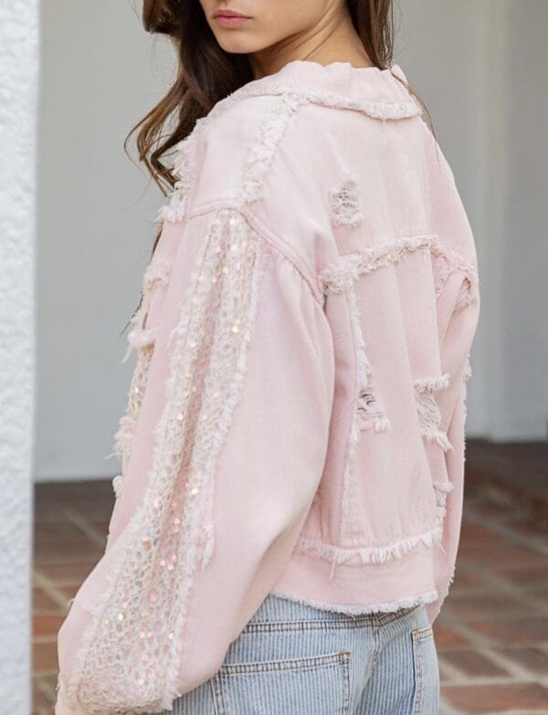 A woman wearing a pink jacket standing next to a wall.