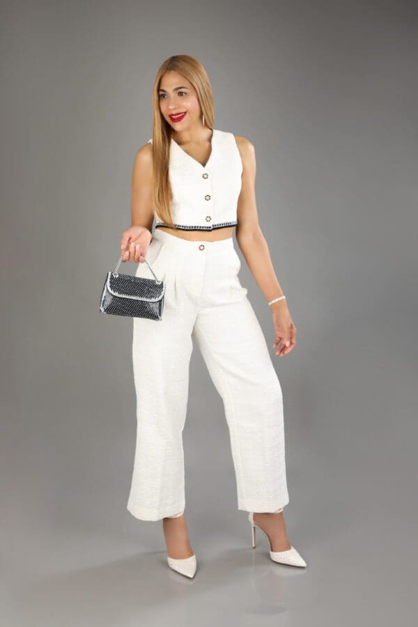 A woman in white outfit holding purse posing for the camera.