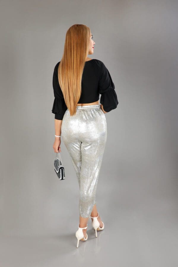 A woman in silver pants and black top holding a camera.