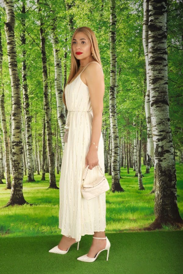 A woman in white dress standing next to trees.