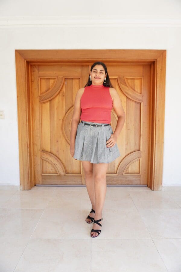 A woman standing in front of a door wearing a skirt.