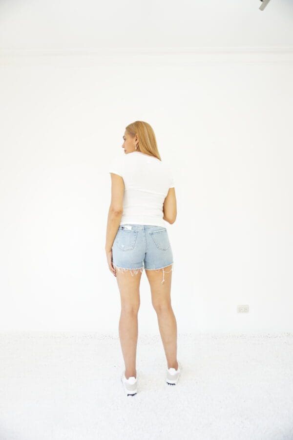 A woman in white shirt and blue shorts standing on top of a wall.