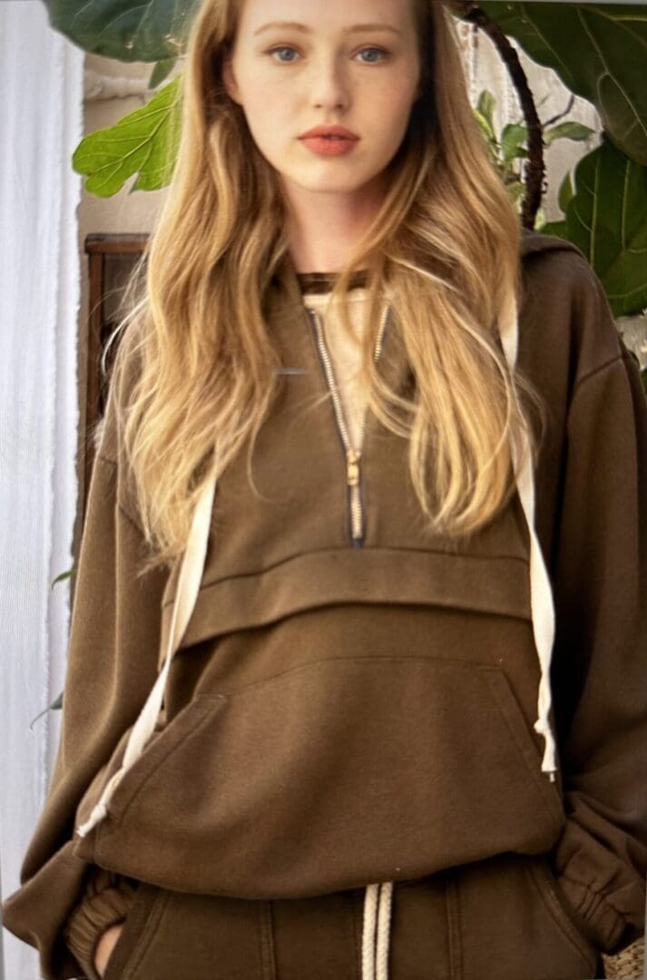 A woman wearing a brown hoodie and smiling.